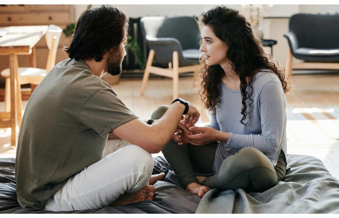 Una pareja sentada en la cama habla con las manos agarradas. Ella tiene gesto de preocupación. Él no muestra el rostro pero por la forma en la que da la mano parece estar preocupado.