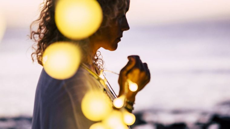 Emotional concept of hope and faith with adult woman and yellow Emotional concept of hope and faith with adult woman and yellow bulb lights defocused - ocean and sunset in background - beautiful portrait for hoping conceptual image